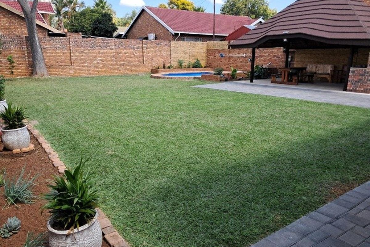 A well-maintained rear garden featuring a lush lawn, a swimming pool, and a covered patio area with brick boundary walls.