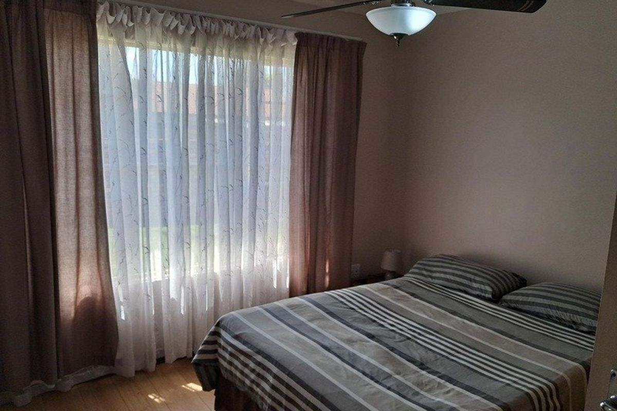 A bedroom featuring laminate flooring, a ceiling fan with integrated lighting, and large windows dressed with curtains.