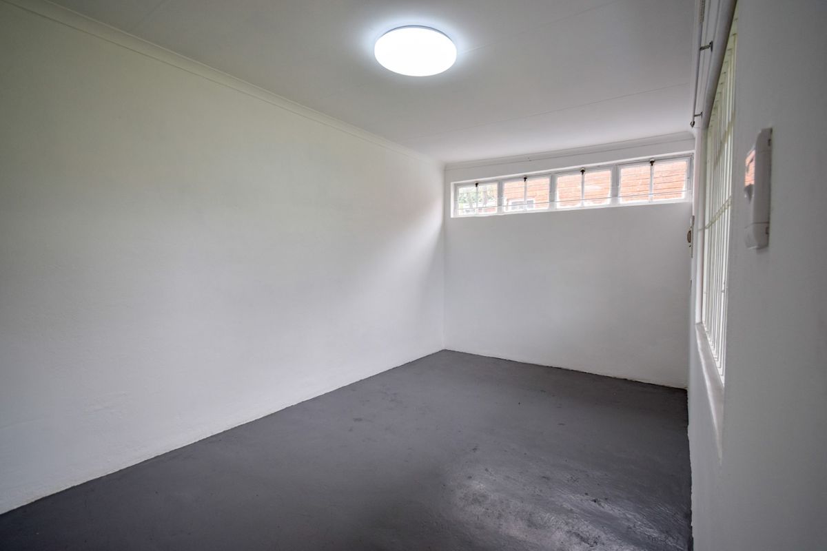 A simple, empty room featuring painted concrete flooring, a ceiling-mounted light fixture, and high-set windows with security bars.