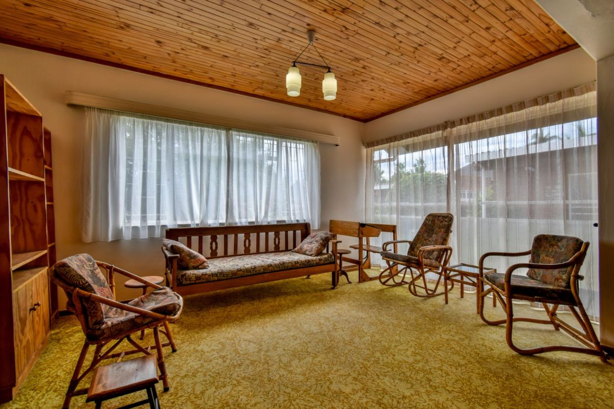 A living room featuring a timber-clad ceiling, large windows with natural light, and carpeted flooring.