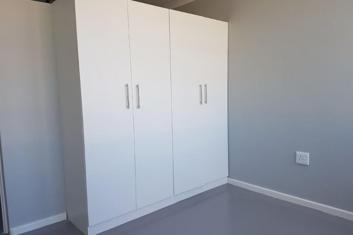 A clean, minimalist bedroom featuring a large white built-in wardrobe and neutral grey flooring and walls.