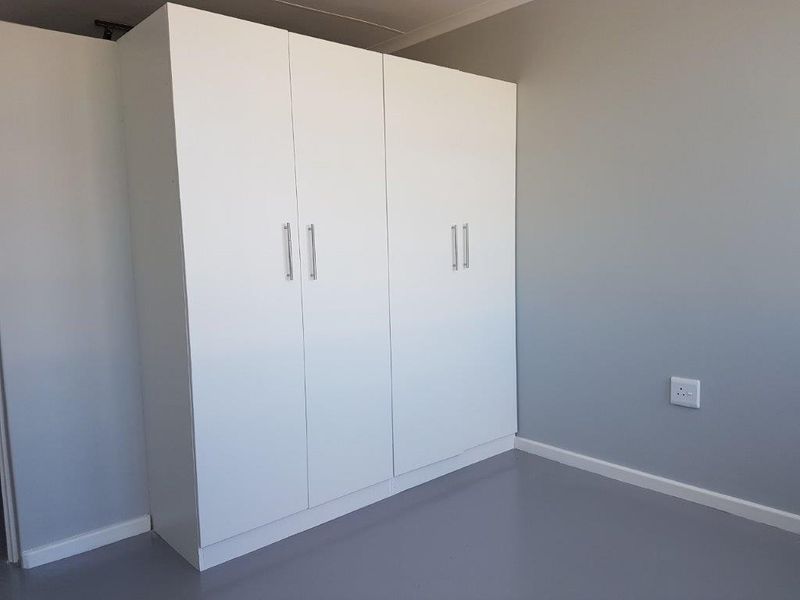 A clean, minimalist bedroom featuring a large white built-in wardrobe and neutral grey flooring and walls.