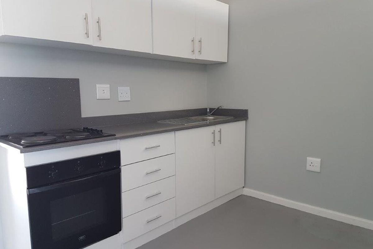 A clean, modern kitchen featuring white cabinetry, dark stone countertops, a built-in oven, and an electric hob.