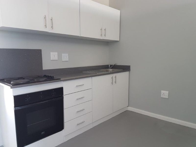 A clean, modern kitchen featuring white cabinetry, dark stone countertops, a built-in oven, and an electric hob.