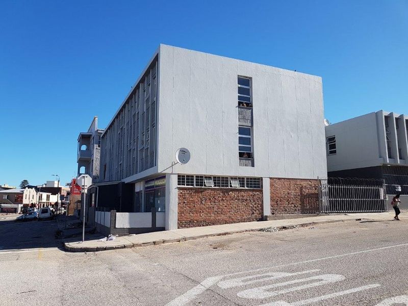 Exterior view of a multi-story apartment building featuring a brick and painted facade, security fencing, and street-level access.
