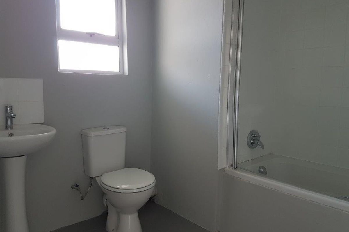A functional bathroom featuring a pedestal basin, toilet, and a bathtub with a shower screen, offering a clean and simple layout.