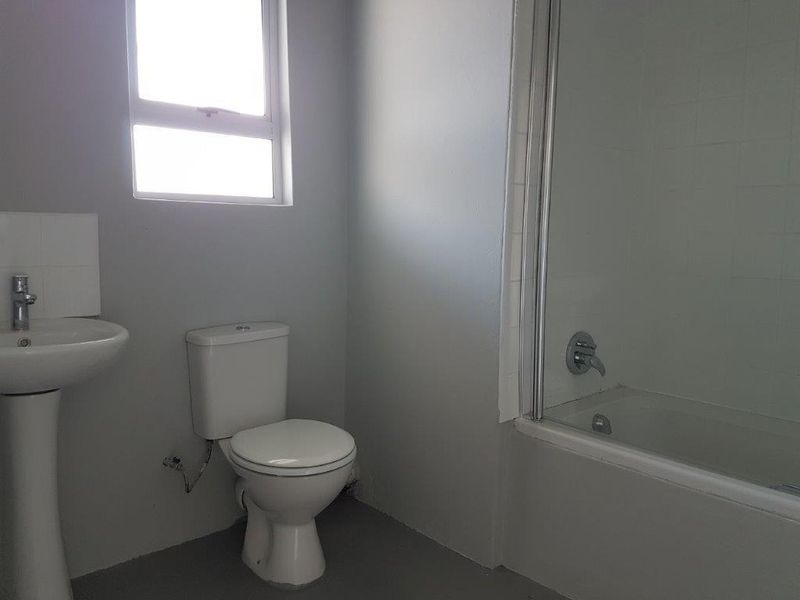 A functional bathroom featuring a pedestal basin, toilet, and a bathtub with a shower screen, offering a clean and simple layout.