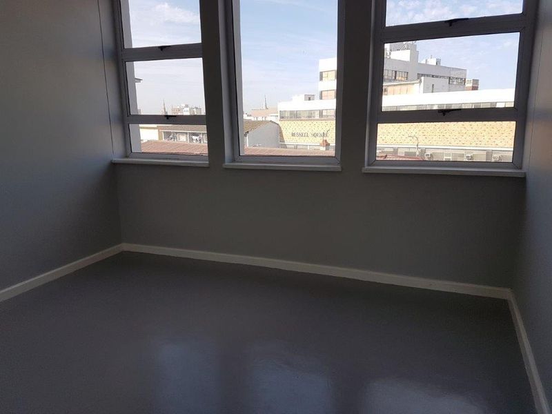 A bright, empty bedroom featuring large windows with urban views, neutral grey walls, and clean flooring, ready for personalization.