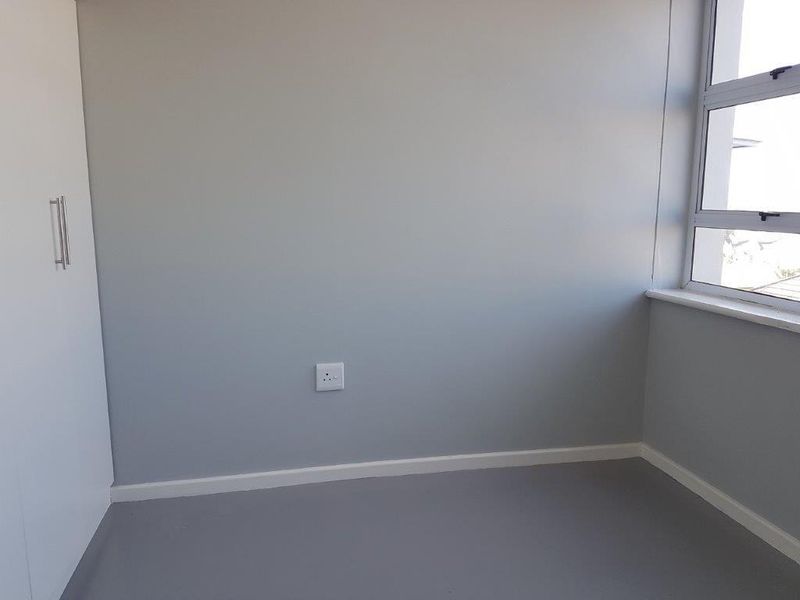 A clean, empty bedroom featuring neutral grey walls, a built-in wardrobe, and large aluminium-framed windows providing natural light.