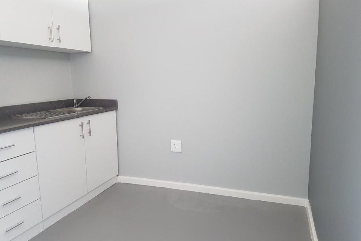 A clean, minimalist kitchen area featuring white built-in cabinetry, a dark countertop, and a stainless steel sink in a neutral-toned space.