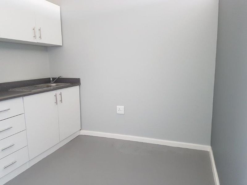 A clean, minimalist kitchen area featuring white built-in cabinetry, a dark countertop, and a stainless steel sink in a neutral-toned space.