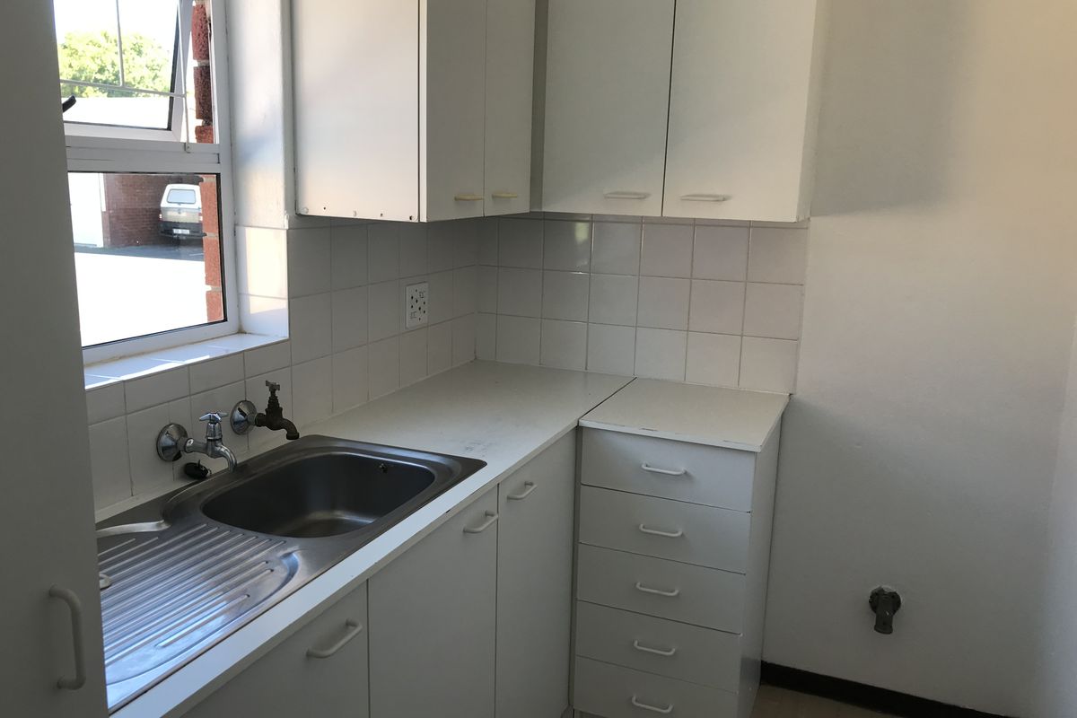 A functional kitchen area featuring white cabinetry, a stainless steel sink, and tiled splashbacks, offering a clean and practical workspace.