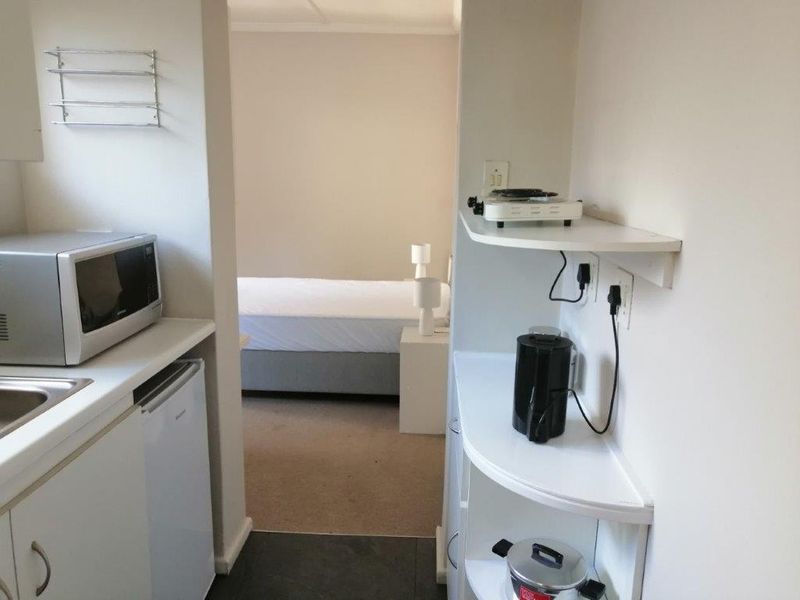 Compact open-plan kitchenette area flowing into a bedroom space, featuring basic built-in shelving and sink unit.