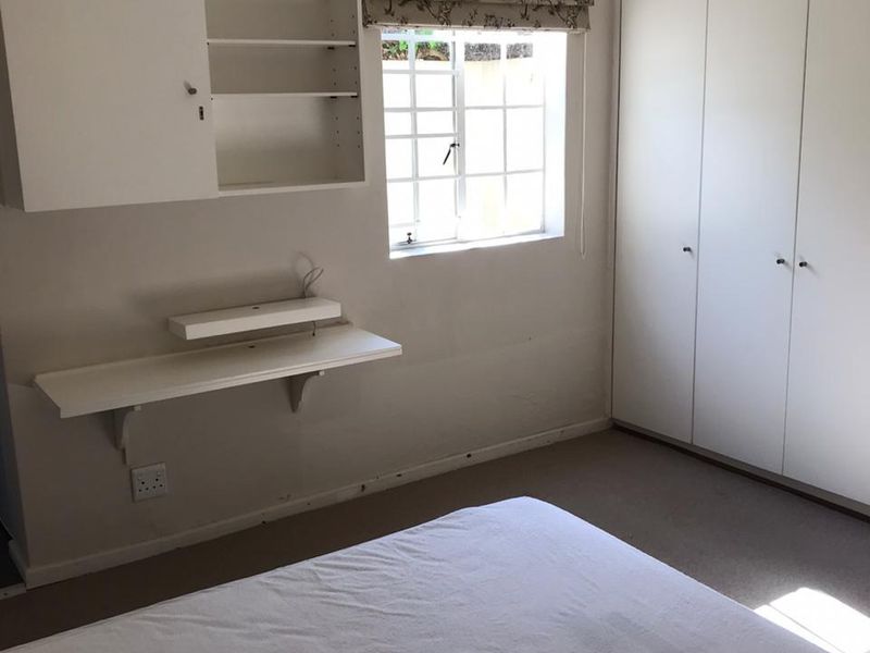 A functional bedroom featuring built-in cupboards, a wall-mounted desk, and shelving, providing practical storage and workspace solutions.