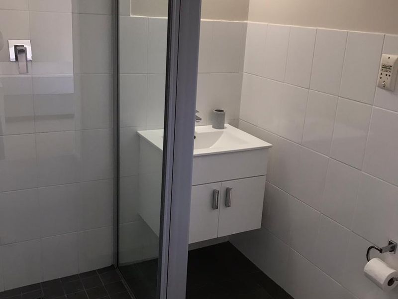 A clean, modern bathroom featuring a wall-mounted vanity, glass-enclosed shower, and neutral tiled finishes throughout.