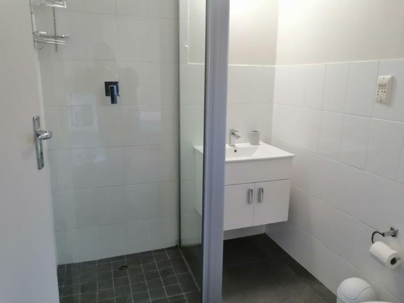 A clean, modern bathroom featuring a walk-in shower with glass screen, wall-mounted vanity unit, and neutral white wall tiling.