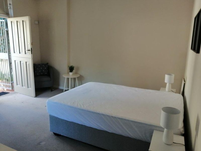 A simple bedroom featuring neutral wall tones, carpeted flooring, and direct access to an outdoor area through a panel door.