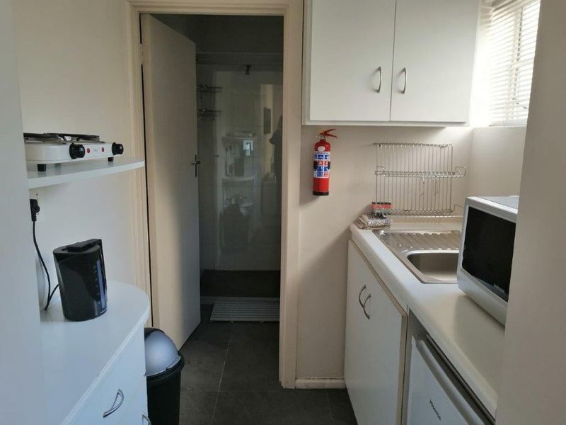 A compact kitchen area featuring white cabinetry, a stainless steel sink, and tiled flooring, with direct access to an adjacent bathroom.