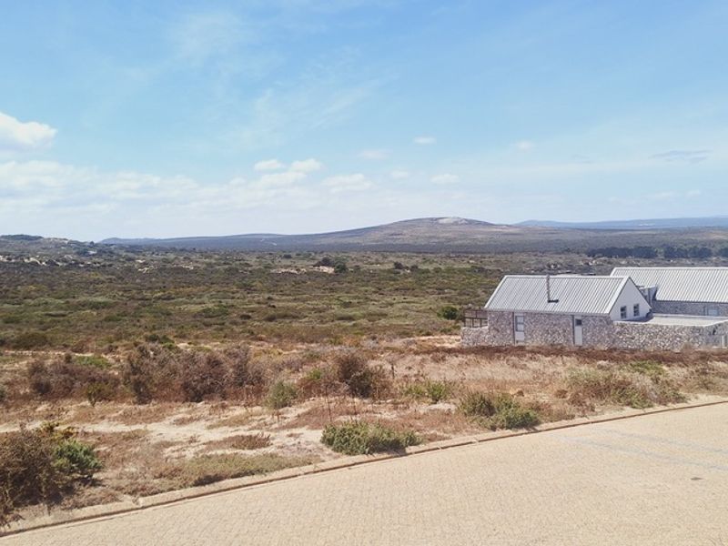 A scenic elevated view overlooking a natural landscape with a stone-clad residential property and paved road in the foreground.