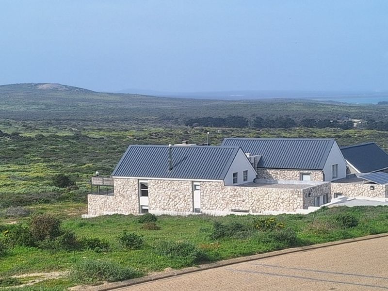 An elevated view of a modern residence featuring stone cladding and a metal roof, set within a natural landscape.