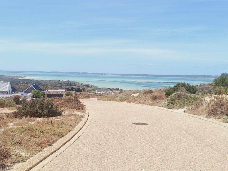 A scenic view of the coastal landscape and lagoon from a paved residential road, showcasing the natural surroundings of the property.