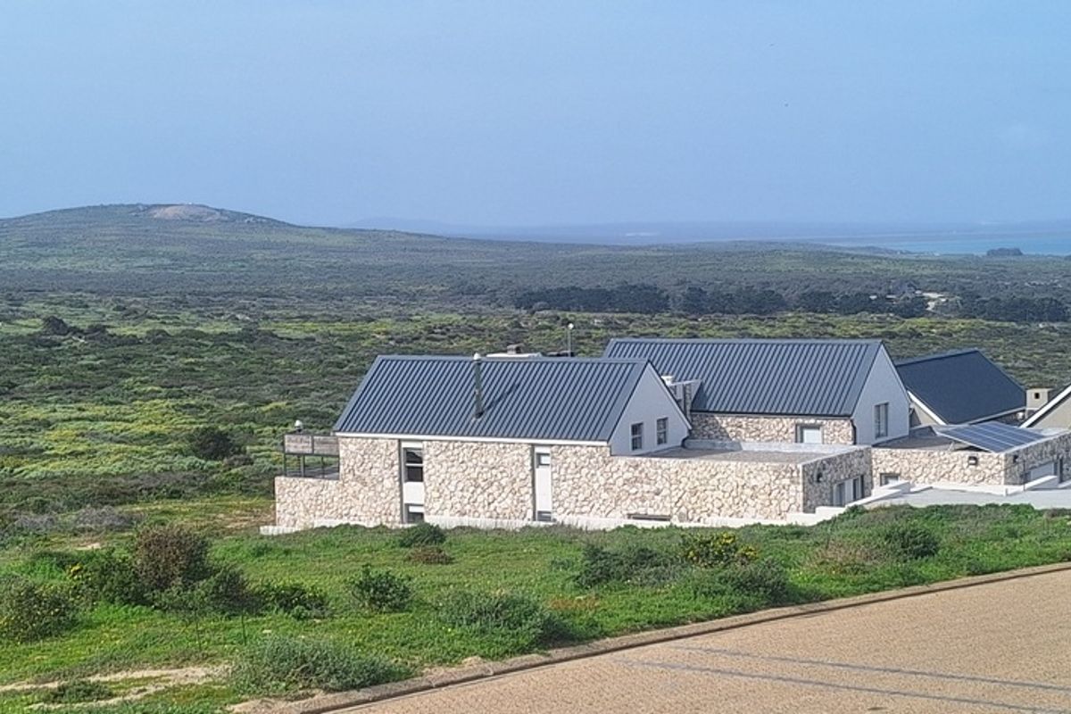 An elevated view of a modern residence featuring stone cladding and a metal roof, set within a natural landscape.