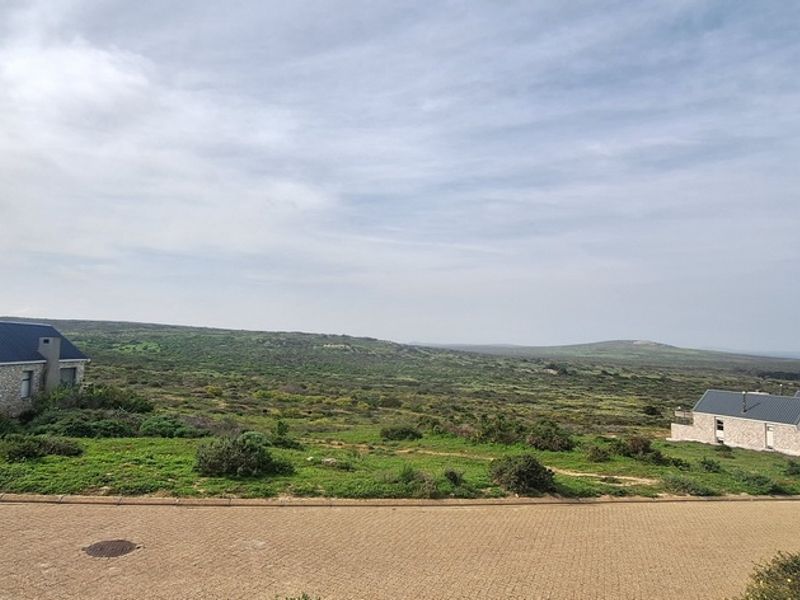 A wide-angle view of the surrounding coastal landscape and neighboring residential properties from a paved street level.