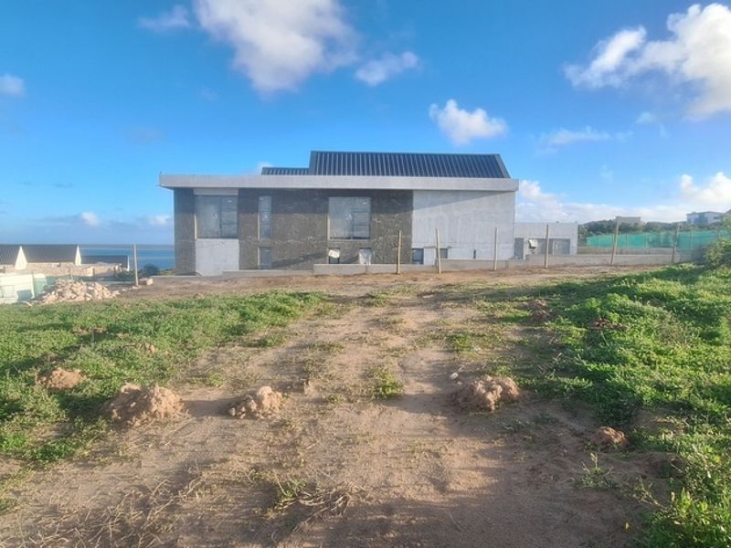 A view of a residential property under construction, featuring stone and plaster exterior finishes and a metal roof, set on a large undeveloped plot.