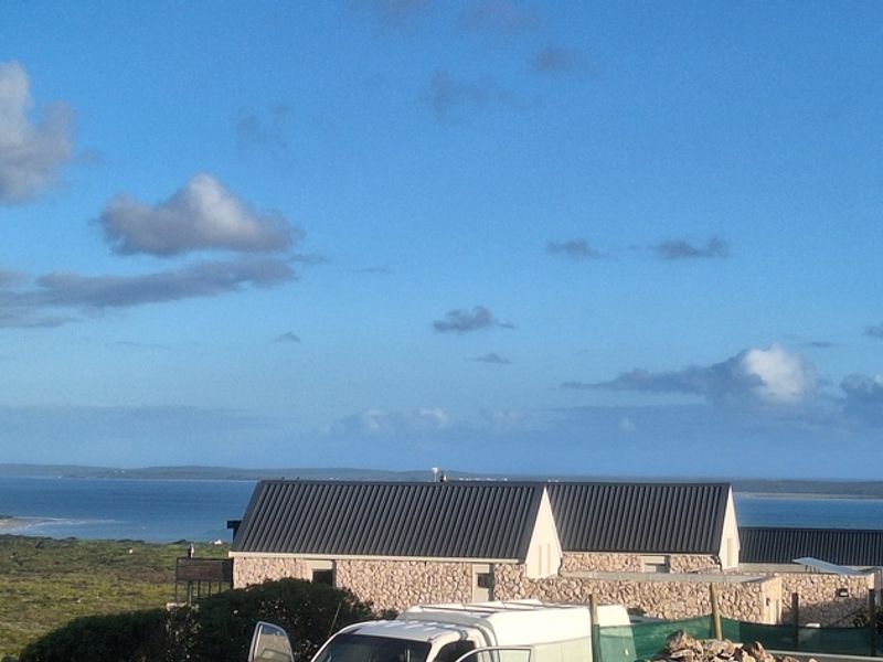A scenic elevated view overlooking a coastal landscape with modern residential buildings featuring stone cladding and metal roofing.