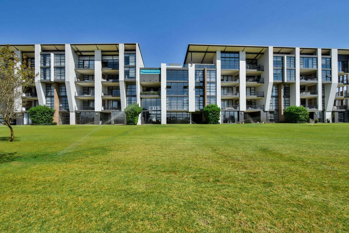 A view of the modern apartment complex facade featuring large glass windows, private balconies, and a well-maintained expansive lawn area.