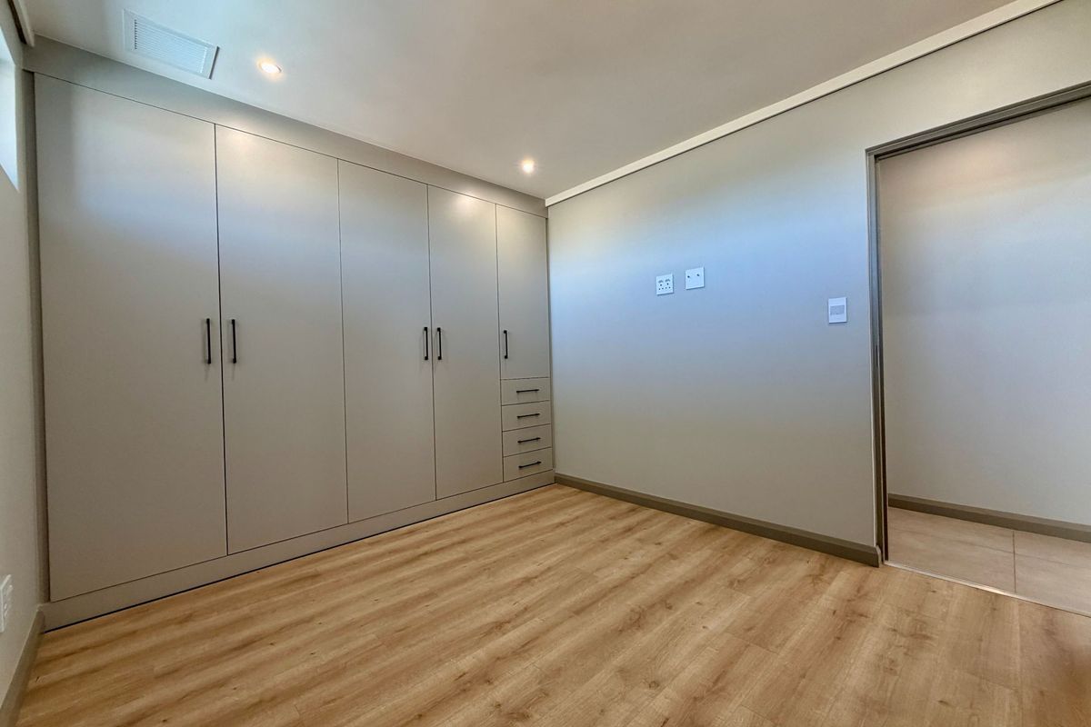 A bright, modern bedroom featuring light wood-look flooring and extensive floor-to-ceiling built-in cabinetry with integrated drawers.
