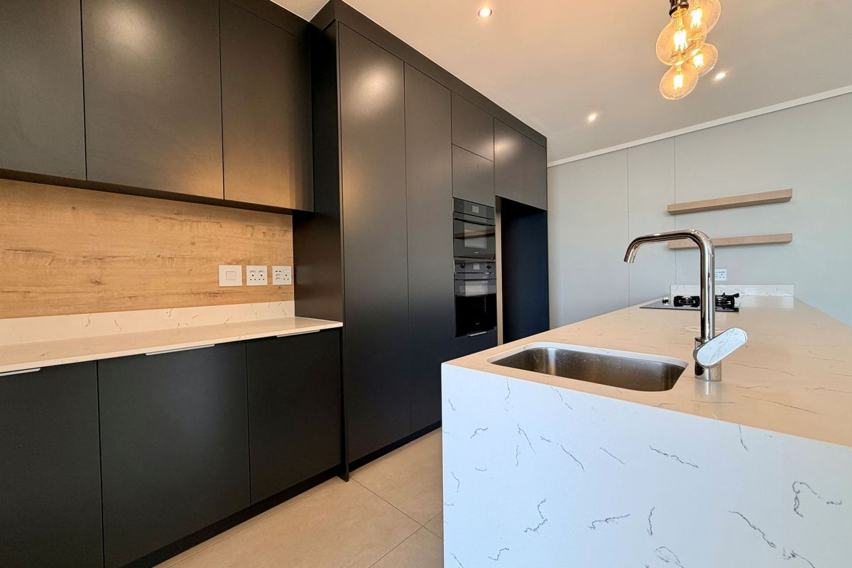 Modern kitchen featuring matte black cabinetry, stone countertops, a central island with a sink, and built-in oven and microwave.
