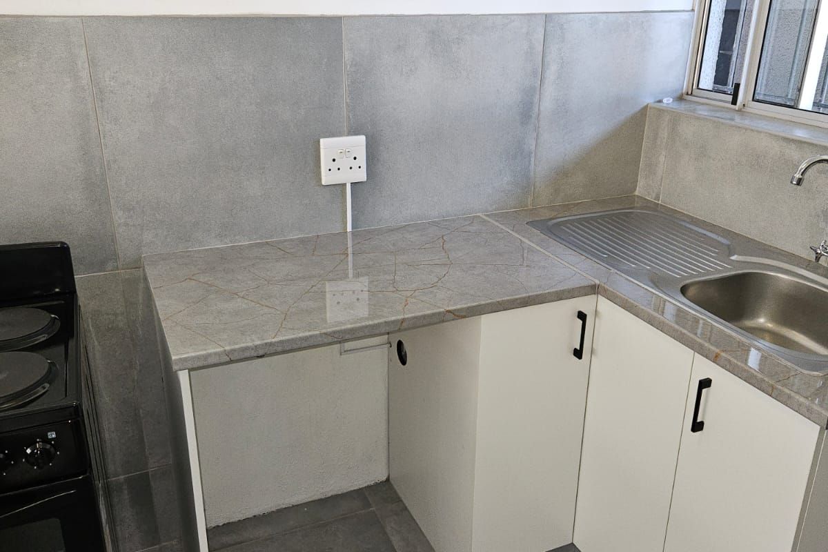 A compact kitchen area featuring modern grey tiled finishes, stone countertops, built-in cabinetry, and a stainless steel sink with mixer tap.