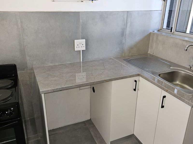 A compact kitchen area featuring modern grey tiled finishes, stone countertops, built-in cabinetry, and a stainless steel sink with mixer tap.