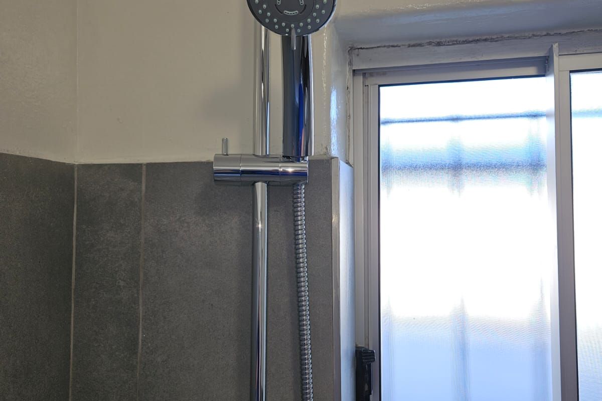 A functional bathroom shower area featuring a modern adjustable shower rail, handheld shower head, and tiled wall finish.