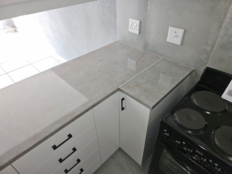 Modern kitchen area featuring sleek white cabinetry, marble-effect countertops, and a built-in electric stove with tiled wall finishes.