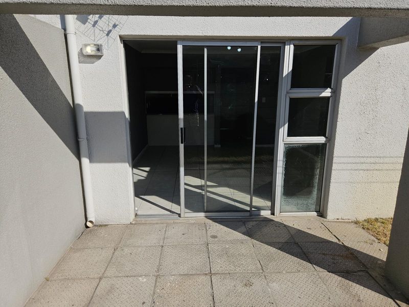 A paved outdoor patio area featuring a sliding glass door entrance and external wall lighting.