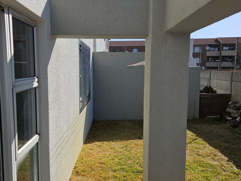 A rear exterior view of the apartment featuring a small lawn, paved patio area, and a structural concrete pergola.