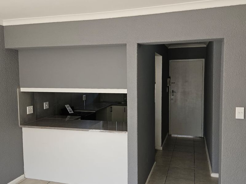 An open-plan living area featuring tiled flooring, a kitchen pass-through counter, and a neutral grey color scheme leading to an internal entrance door.