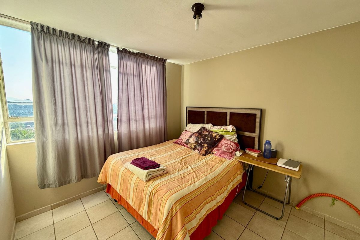 A bedroom featuring tiled flooring and a large window with curtains, providing natural light and views.