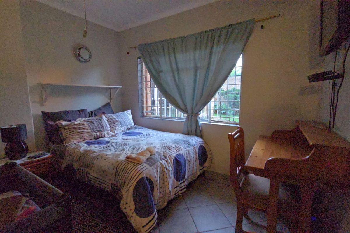 A functional bedroom featuring tiled flooring, a built-in wall shelf, and security bars on the window.