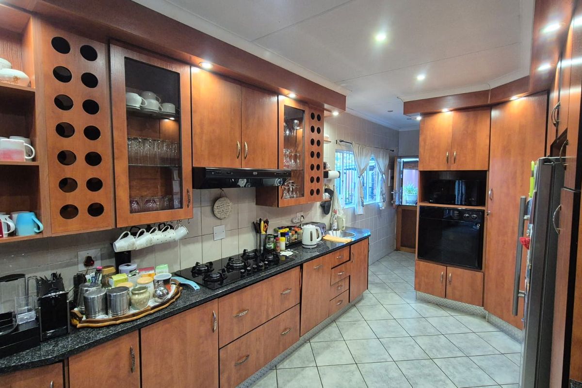 A functional kitchen featuring wood-finish cabinetry, granite countertops, a built-in oven, gas hob, and tiled flooring with recessed ceiling lighting.