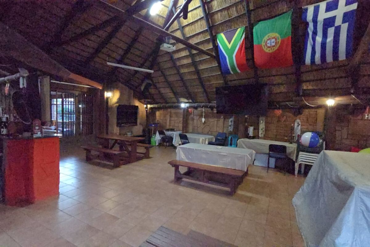 Spacious entertainment area featuring a high-pitched thatch roof, exposed timber beams, tiled flooring, and a built-in bar counter.