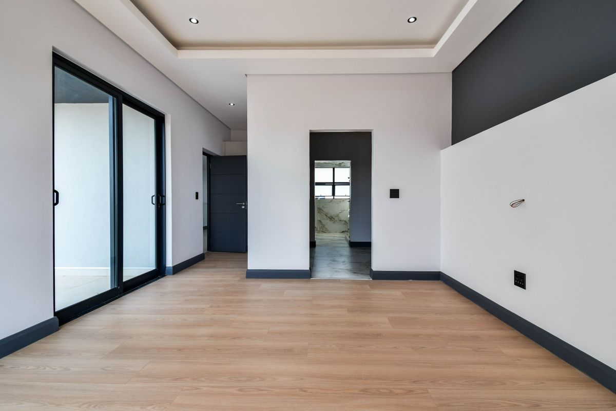 A modern, empty living space featuring light wood-look flooring, recessed ceiling lighting, and sliding glass doors leading to an outdoor area.