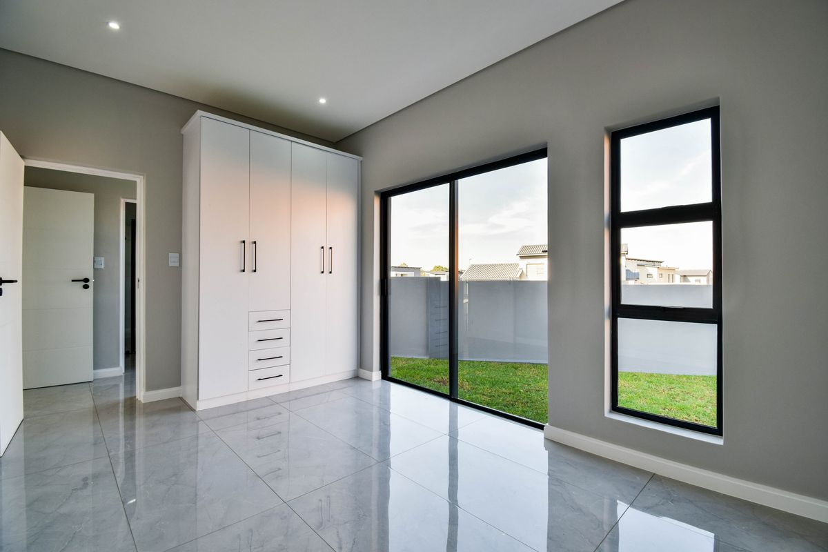 Modern bedroom featuring sleek grey tiled flooring, built-in white cabinetry, and large sliding glass doors providing direct access to the garden.
