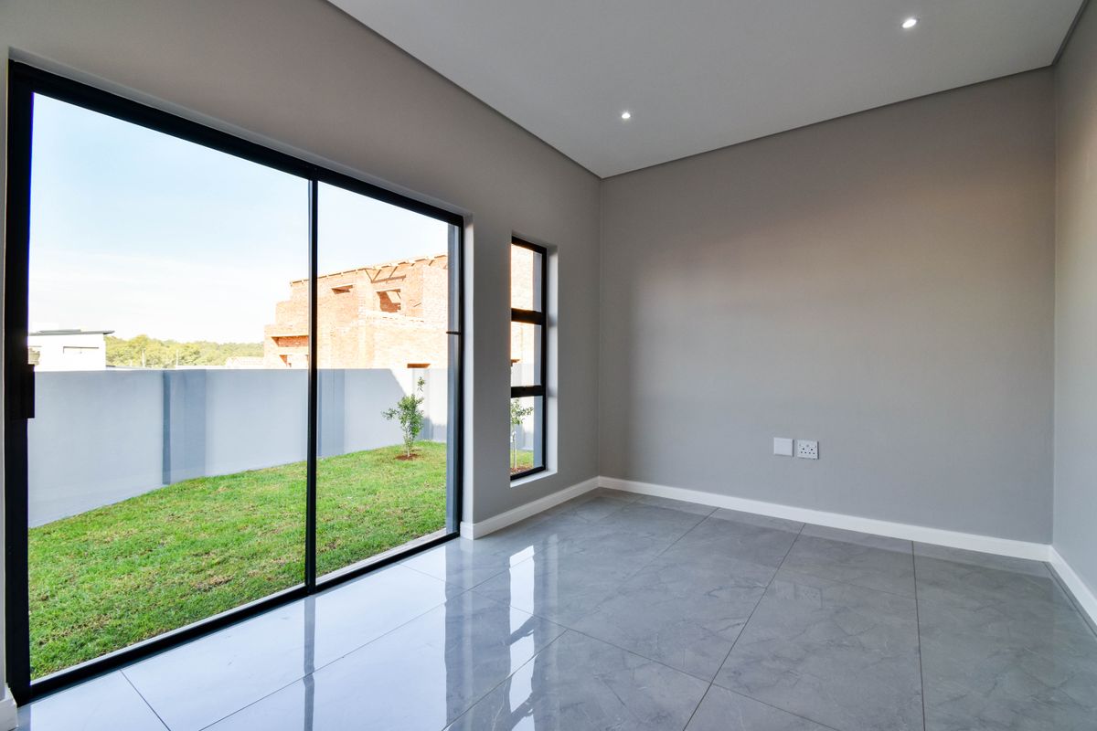 A bright, modern living room featuring large sliding glass doors, polished porcelain floor tiles, recessed downlighting, and direct access to a private garden.