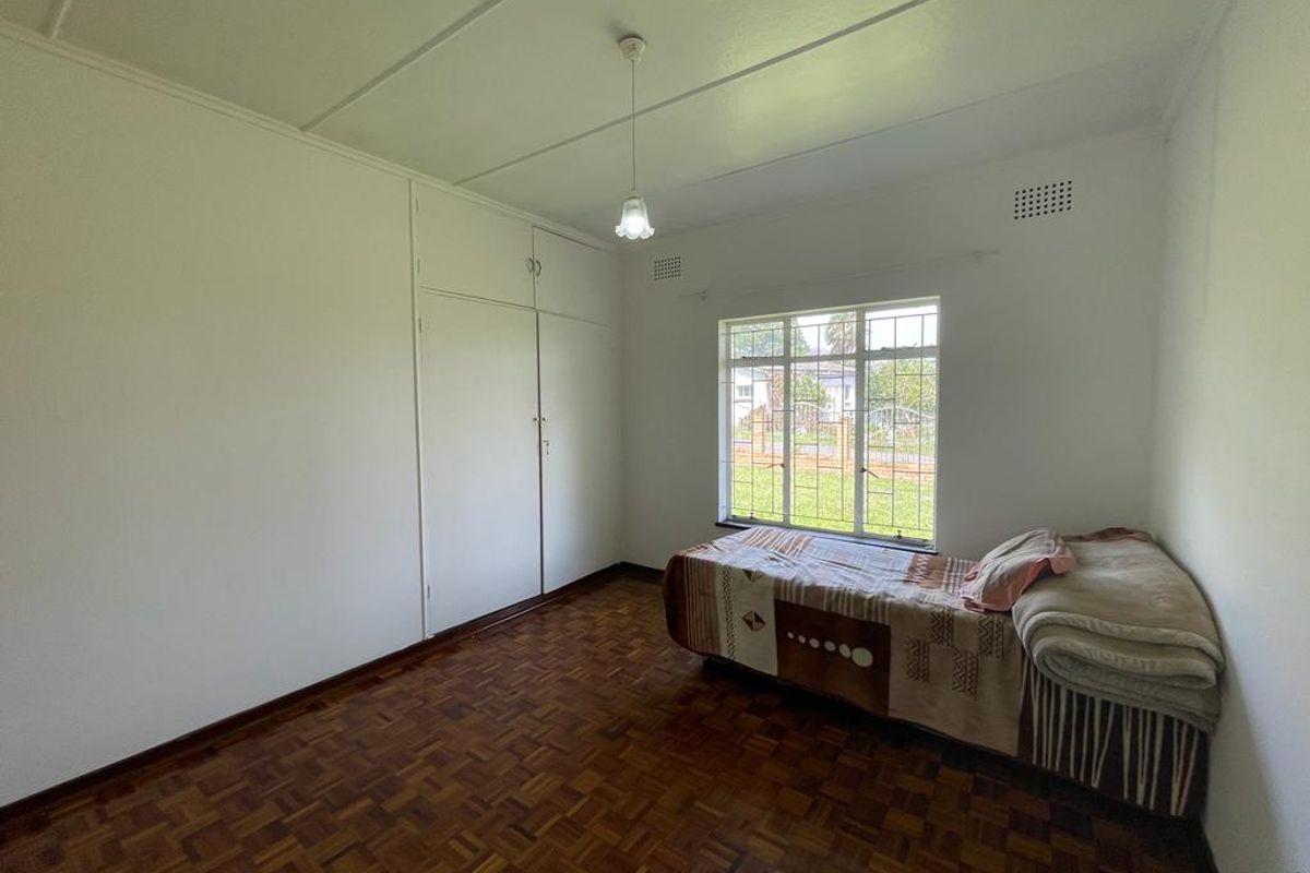 A bedroom featuring original parquet flooring, built-in cupboards, and a large window providing natural light and garden views.