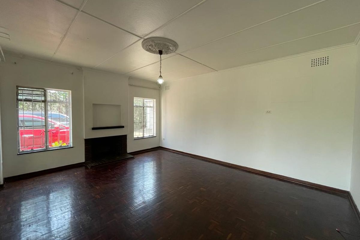 Spacious living room featuring original parquet flooring, a built-in fireplace, and decorative ceiling rose with pendant lighting.