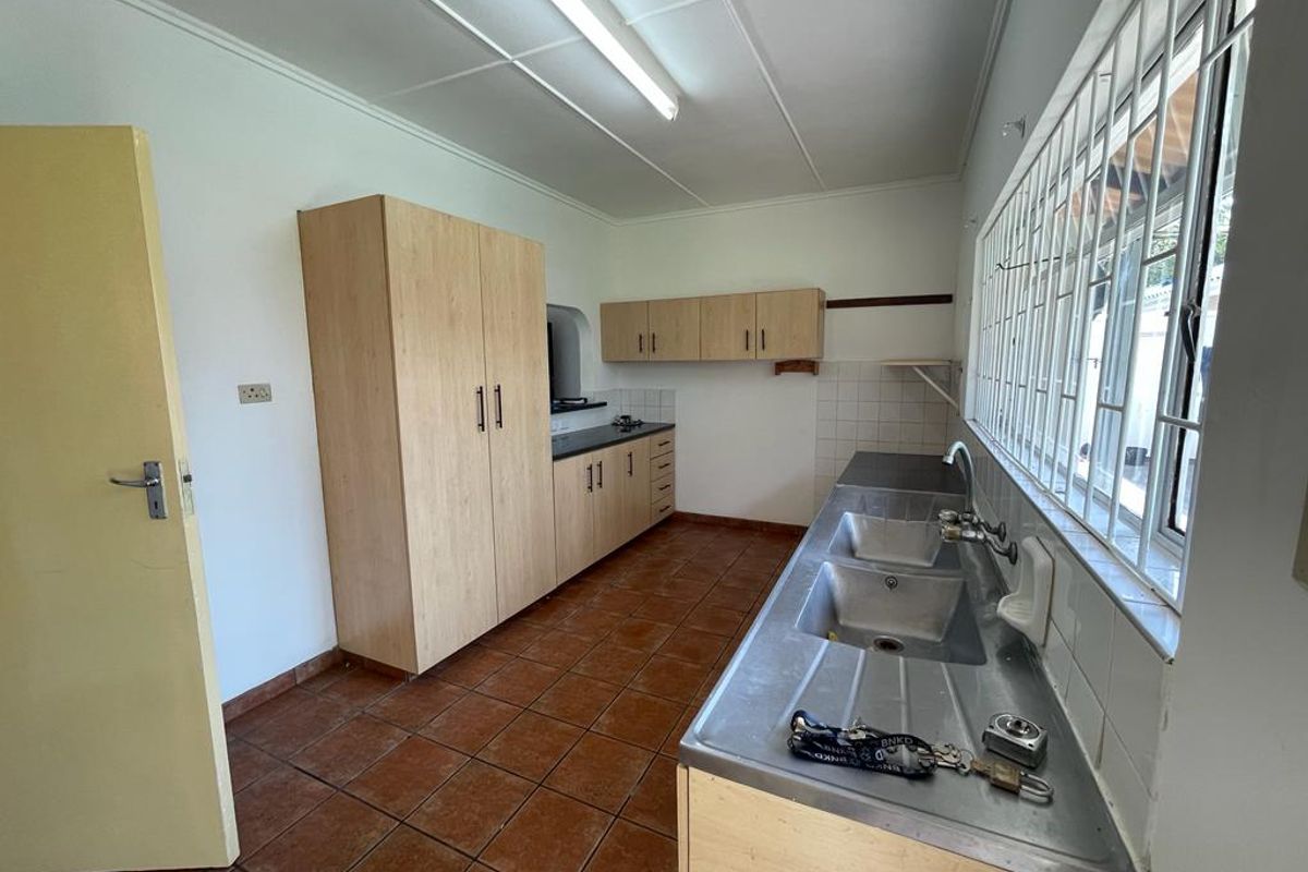 A functional kitchen featuring light wood cabinetry, a double stainless steel sink, and tiled flooring with large windows providing natural light.