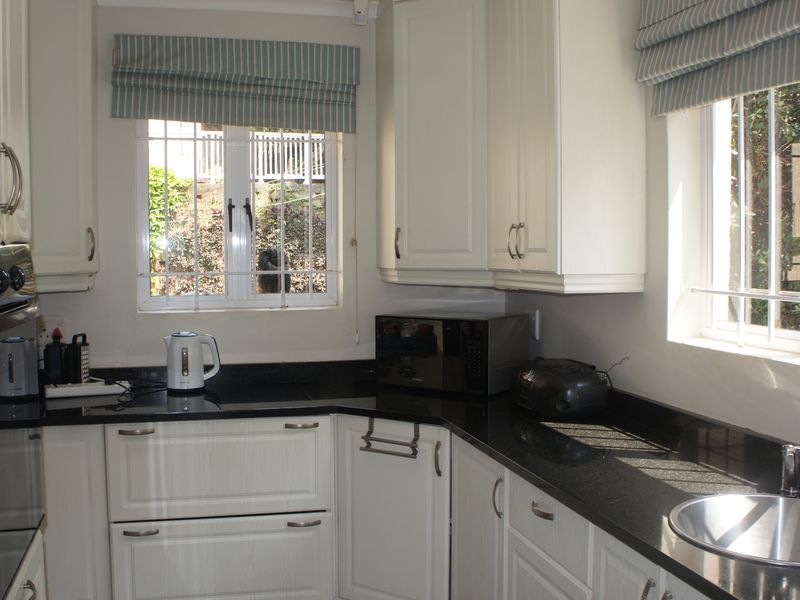 A functional kitchen featuring white shaker-style cabinetry, dark granite countertops, a built-in oven, and stainless steel sink with security bars on the windows.